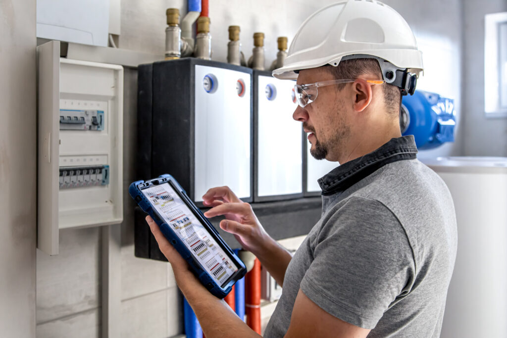 Elektriker prüft Schaltschrank mit Tablet.